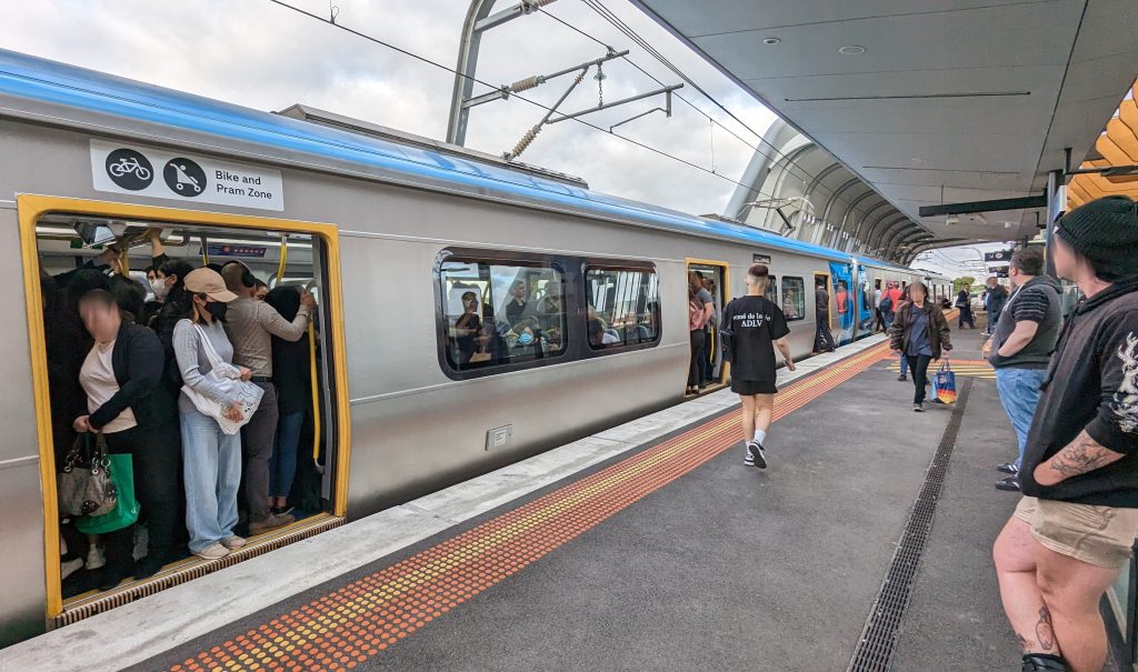 Crowded train waiting at a platform. Some passengers have chosen not to board.