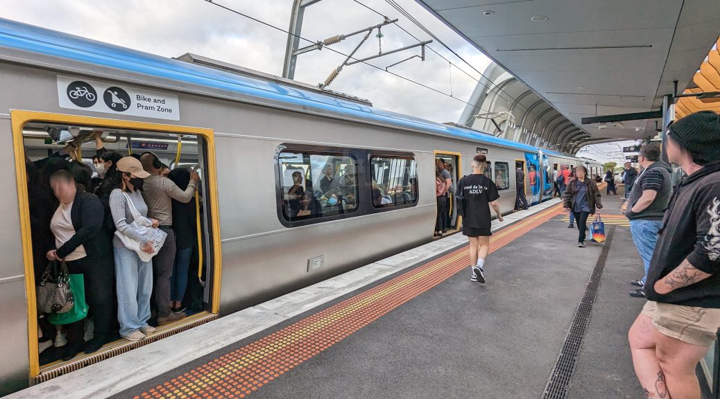 Crowded train waiting at a platform. Some passengers have chosen not to board.